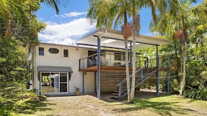 A modern house with a covered patio, a wooden deck, and a staircase leading to an upper level.