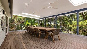 A covered outdoor dining area with a wooden table and chairs, surrounded by lush greenery.