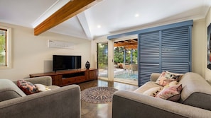 A spacious living room with a flat-screen TV, wooden entertainment unit, and two sofas with cushions. - Salty Seaside - by Lifestyle. Brunswick Heads (NEW BRIGHTON)