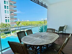 Un balcon avec une table et des chaises en bois, donnant sur une piscine et offrant une vue sur la ville.