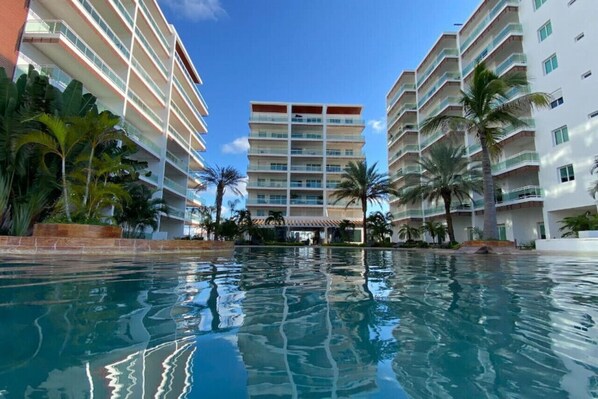 Un hôtel à plusieurs étages, doté d’une piscine et bordé de palmiers.
