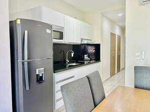 A modern kitchen with a built-in refrigerator, microwave, and sink. There are grey chairs and a wooden table.