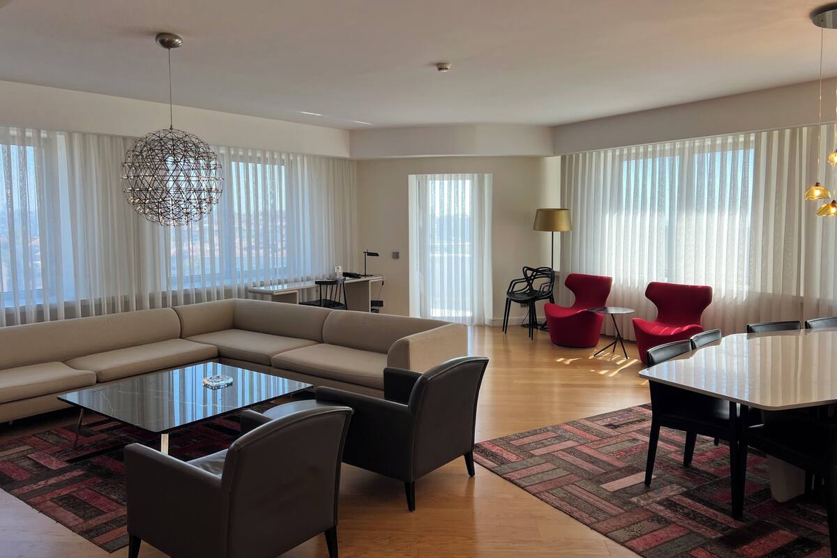 A modern living room with a sectional sofa, a glass coffee table, and a dining area with a white table and chairs.