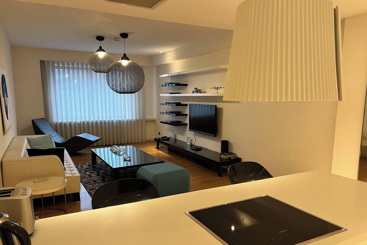 A modern living room with a sofa, a coffee table, a TV, and a kitchen area with a stove.