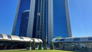 A modern high-rise building with reflective glass windows and a curved glass canopy structure in the foreground. - Akmerkez Residence (Istanbul)