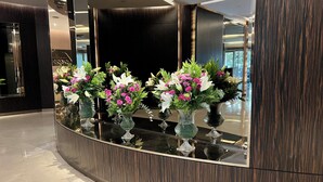 A reception area with a curved reception desk, multiple vases with flowers, and a dark wood paneling wall. - Akmerkez Residence (Istanbul)