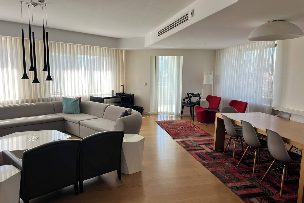 A modern living room with a sectional sofa, a dining table with chairs, and a kitchen area in the background.