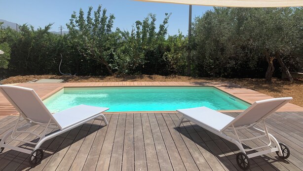 Une terrasse en bois avec une piscine, deux chaises longues blanches et un auvent pour faire de l’ombre.