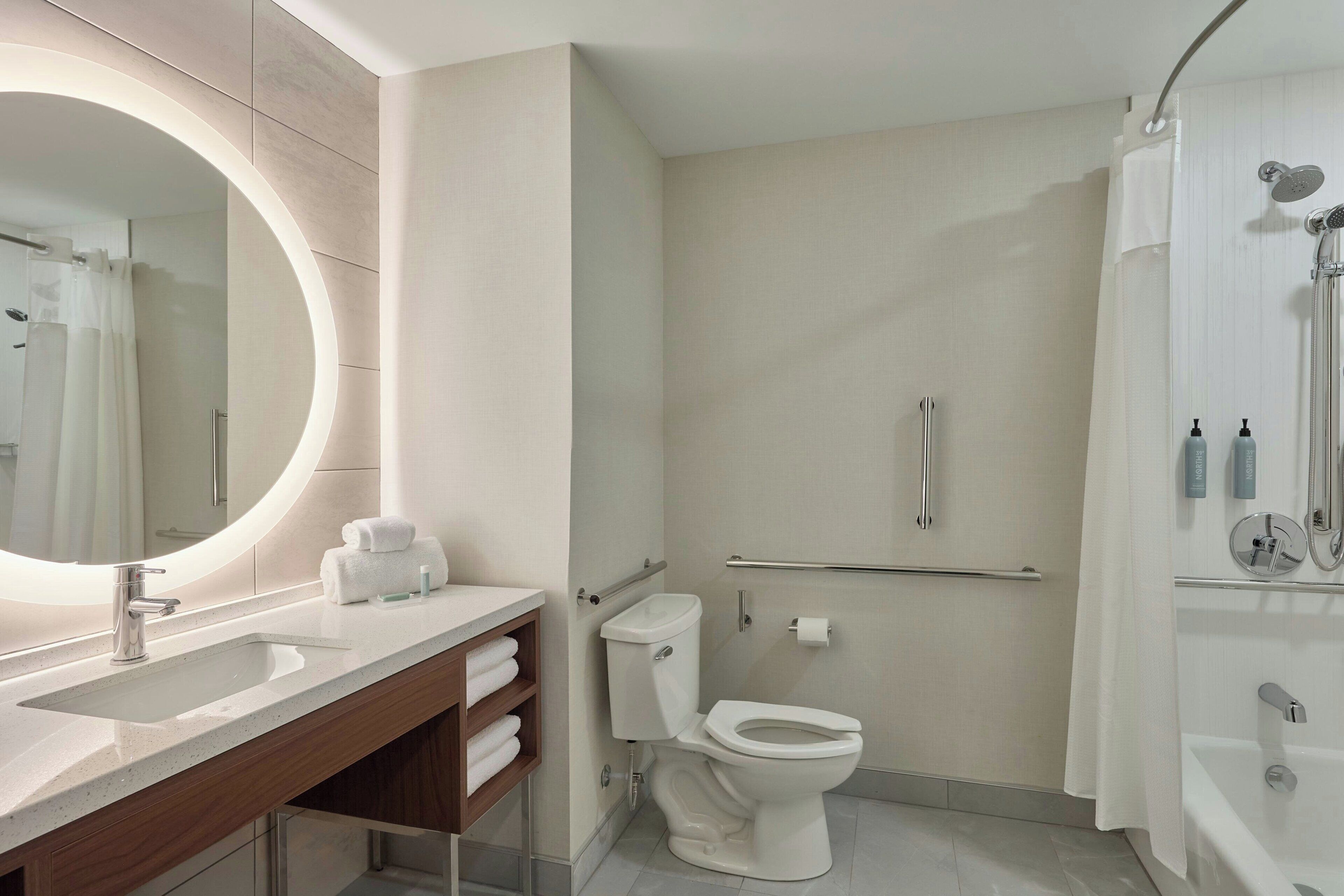 A modern bathroom with a large mirror, a sink, a toilet, and a shower area.