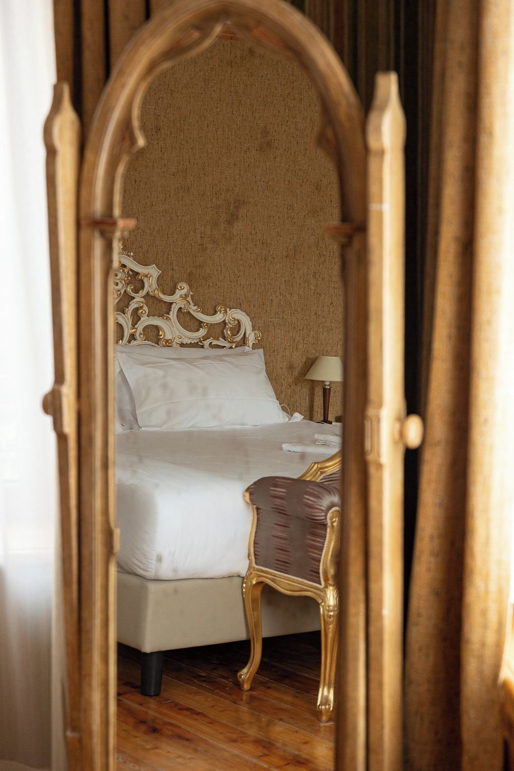 Un letto con lenzuola bianche, una testiera in legno e un comodino con una lampada.