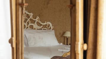 Un letto con lenzuola bianche, una testiera in legno e un comodino con una lampada.