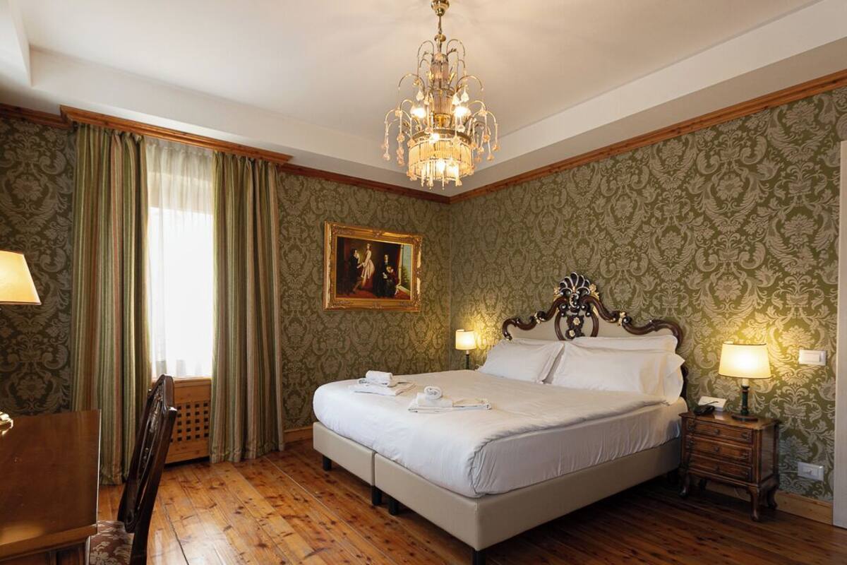 Una habitación de hotel con una cama grande, suelo de madera, un candelabro, un escritorio y una silla.