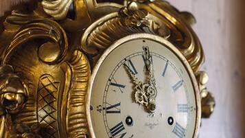 Eine aufwendige, antike Uhr mit römischen Ziffern vor einem Holzhintergrund.