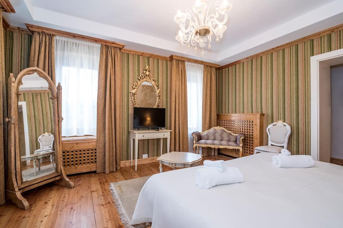 Habitación de hotel con una cama grande, televisor, tocador con espejo y dos sillones.