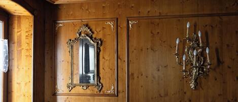 A dining room with wooden paneling, a chandelier, ornate mirror, and a table with chairs.