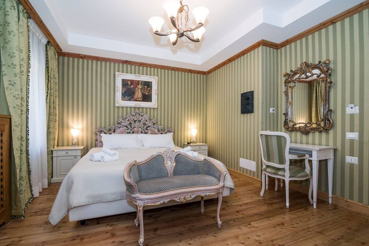 Un dormitorio con cama, una silla, un escritorio, un espejo y una ara ña.