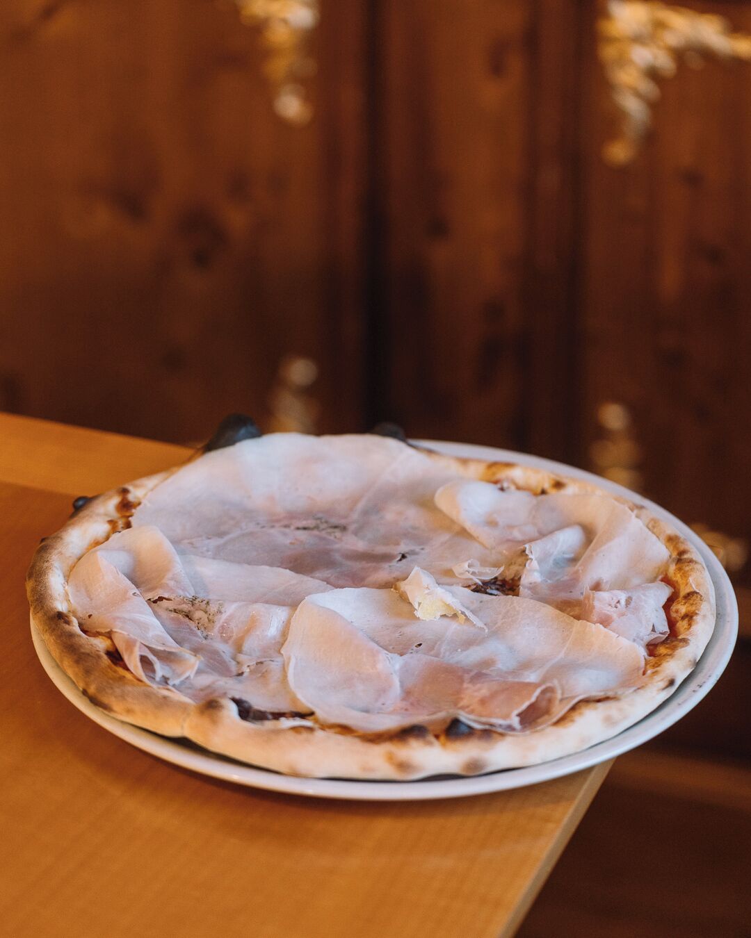 Una pizza sobre un plato blanco en una mesa de madera.
