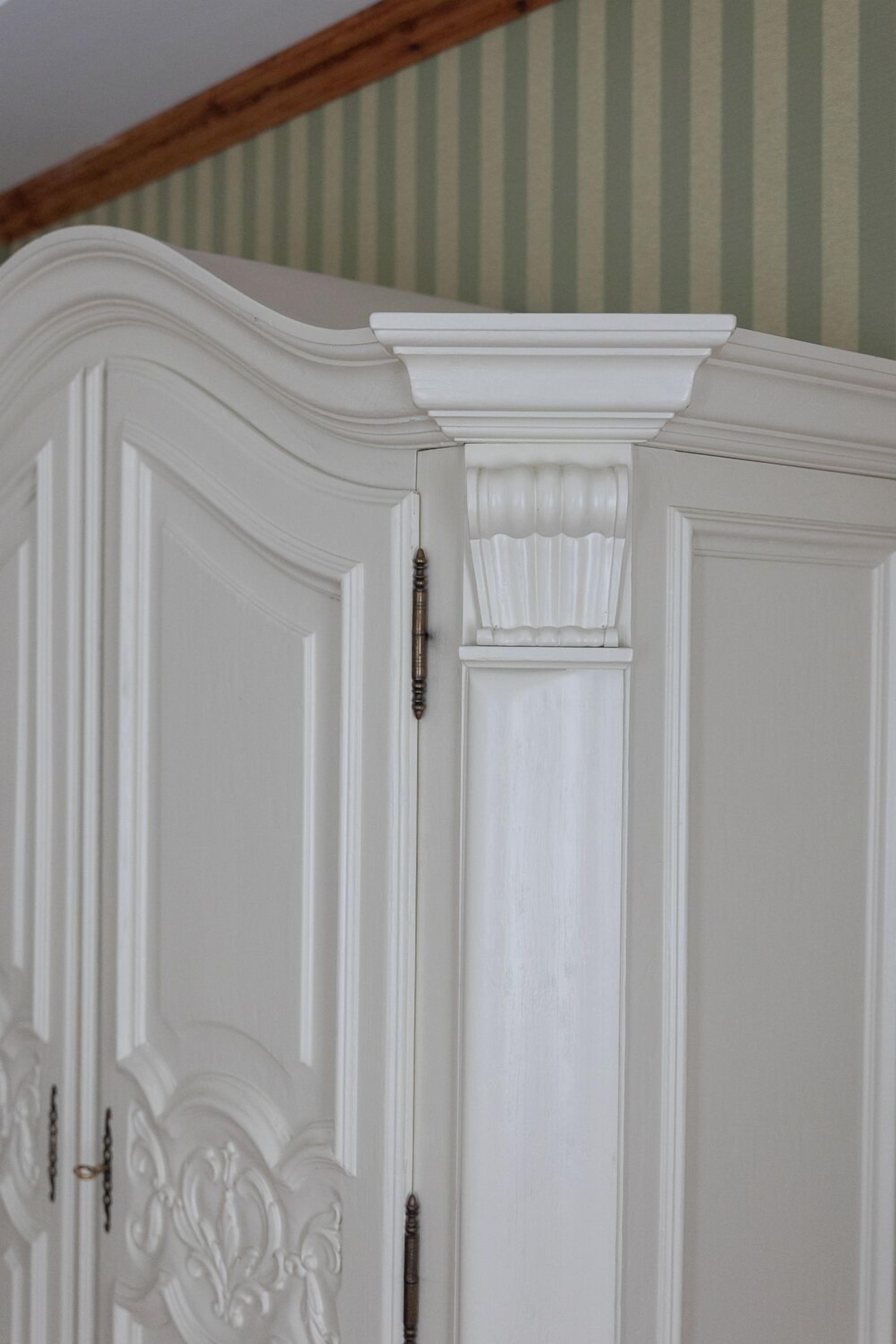 Un armario blanco y ornamentado con elaboradas tallas y un tirador de latón.