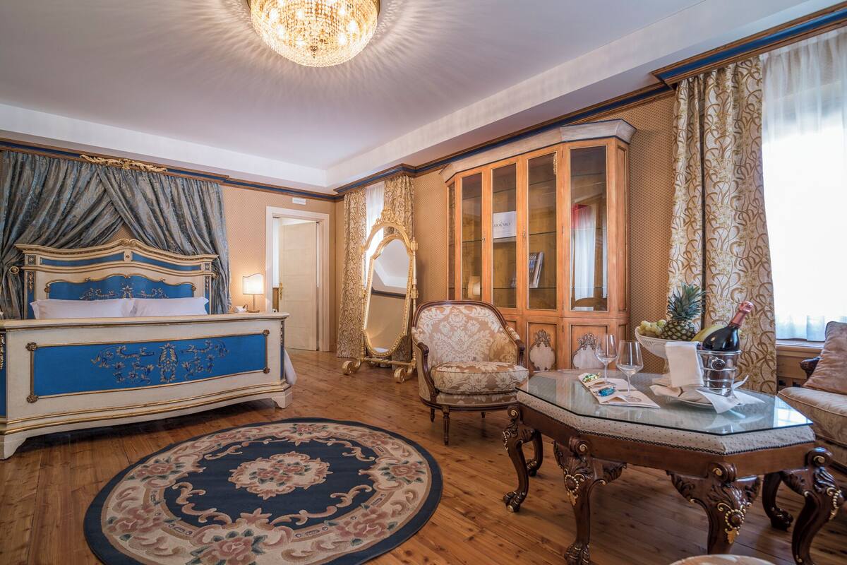 Una habitación lujosa con una cama grande, muebles ornamentales, una mesa de cristal y un aparador de madera.