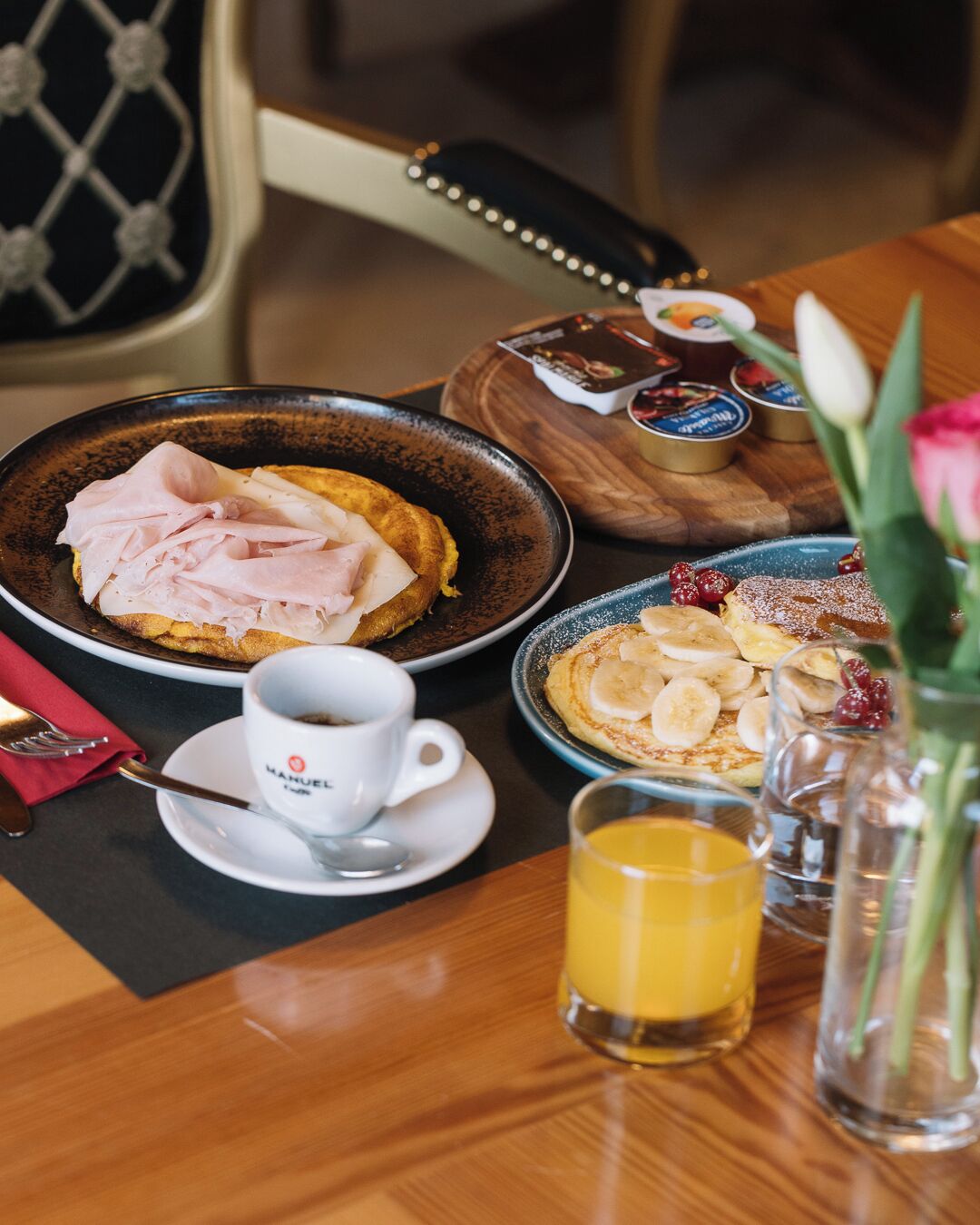 A breakfast setting with plates of food, a cup of coffee, a glass of orange juice, and a vase with flowers.