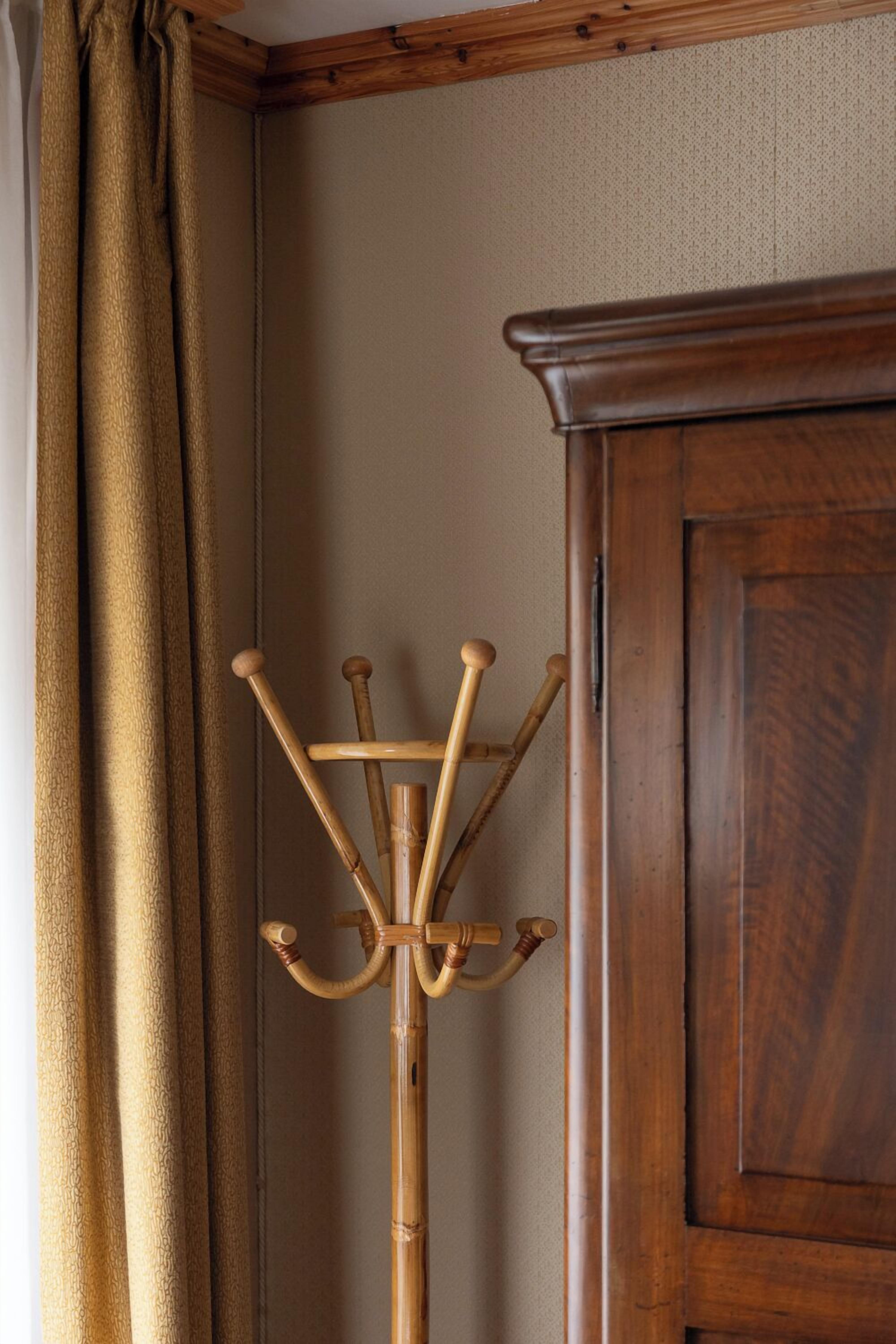 A wooden coat rack with multiple hooks, positioned next to a wooden door and a beige curtain.
