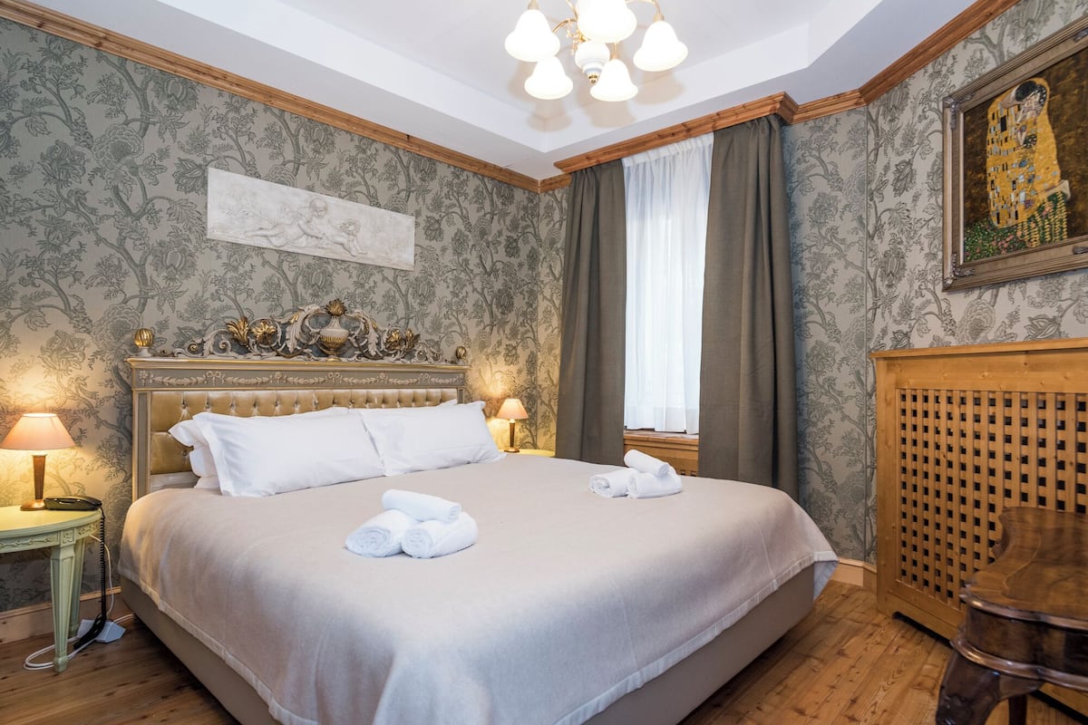 Una habitación de hotel con una cama grande, un cabecero de madera, una mesita de noche con una lámpara y un cuadro en la pared.