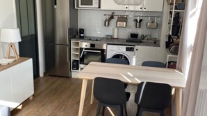 Une cuisine compacte dotée d’appareils électroménagers modernes, un coin repas avec une table et des chaises, et un vase décoratif contenant des plantes séchées.