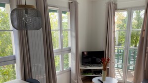 Un salon moderne comprenant une table à manger, des chaises, un canapé, un téléviseur et de grandes fenêtres avec des rideaux.