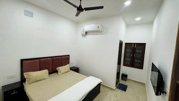 Un dormitorio con cama, mesitas de noche, ventilador de techo, unidad de aire acondicionado, televisor y puerta con ventana.
