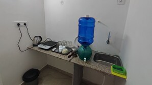 Una pequeña cocina equipada con dispensador de agua, hervidor, balanza y lavamanos.