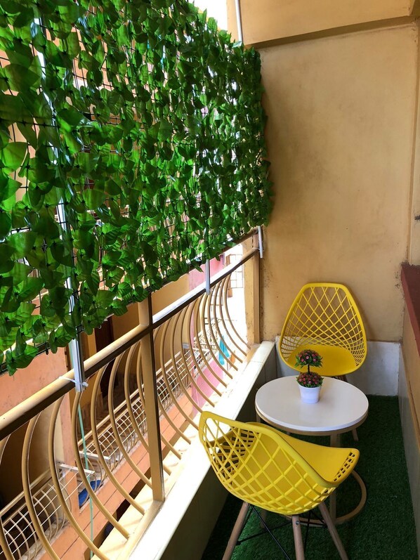 A balcony with a green leafy wall, yellow chairs, and a small table with a potted plant. - Lux Suites Father's Hub Apartments (Nairobi)