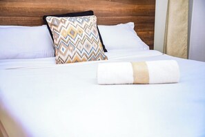 A neatly made bed with a patterned pillow and a rolled towel. - Lux Suites Father's Hub Apartments (Nairobi)