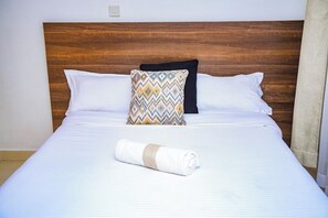 A neatly made bed with a patterned pillow, white linens, and a rolled towel. - Lux Suites Father's Hub Apartments (Nairobi)