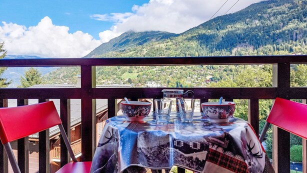 Uma mesa com toalha, duas cadeiras vermelhas e uma vista panorâmica das montanhas.