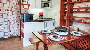 Cozinha compacta com micro-ondas, torradeira e cafeteira. Uma mesa de jantar está posta com pratos e talheres.