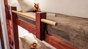 Uma cama beliche com escada de madeira, um brinquedo de pelúcia no colchão superior e um pequeno brinquedo no chão.