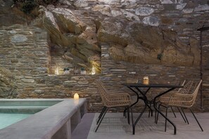 Un muro de piedra con una zona de estar integrada, una piscina y una mesa con sillas.