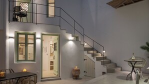 A modern interior with a staircase, a dining area with wicker chairs, a small table with a candle, and a pool area. - Porto Sereno Andros Suites (Andros)