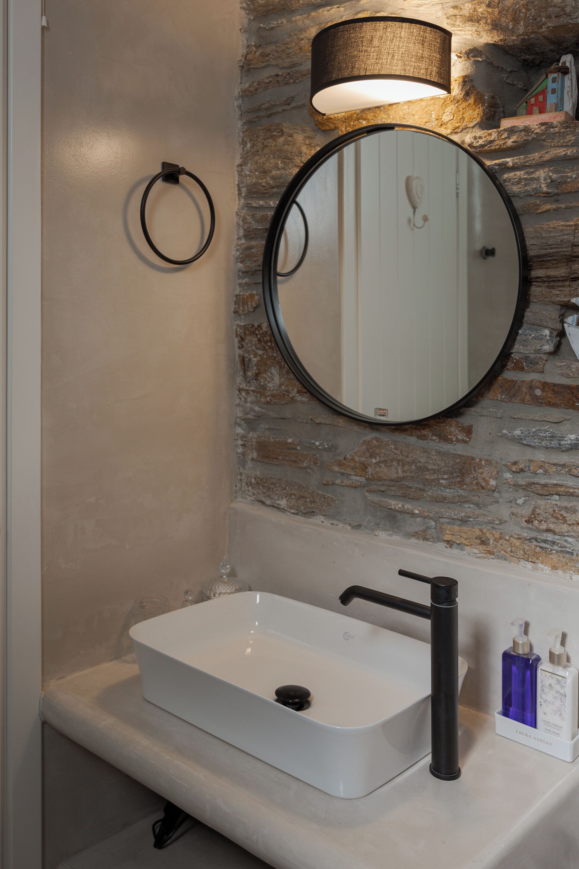 Un baño con lavamanos blanco, grifo negro y un espejo redondo con luz superior.