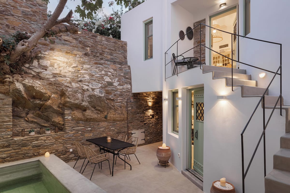 Una casa moderna con un muro de piedra, un área de comedor con sillas, una mesa y una piscina pequeña.