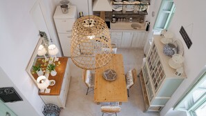 A compact kitchen with a wooden table, wicker chairs, and a hanging light fixture. - Porto Sereno Andros Suites (Andros)