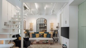 A spacious living room with a staircase, a sofa set, a coffee table, and a television. - Porto Sereno Andros Suites (Andros)
