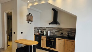 A modern kitchen with a wooden table, black cabinets, and a black range hood. - Aristotle Suites, Aura (Adamantas)