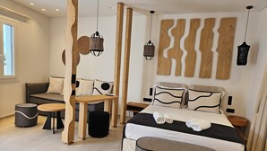 A modern bedroom with a bed, bedside tables, a sofa, and a dining area. - Aristotle Suites, Aura (Adamantas)