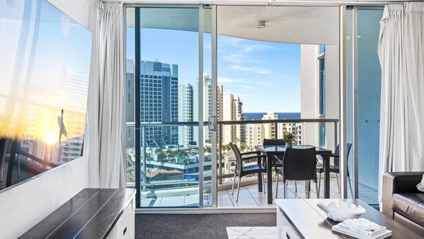 A modern hotel room with a large sliding glass door leading to a balcony with a city view.
