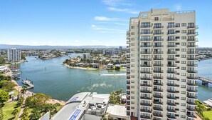 A high-rise hotel with multiple balconies, overlooking a body of water and a marina.