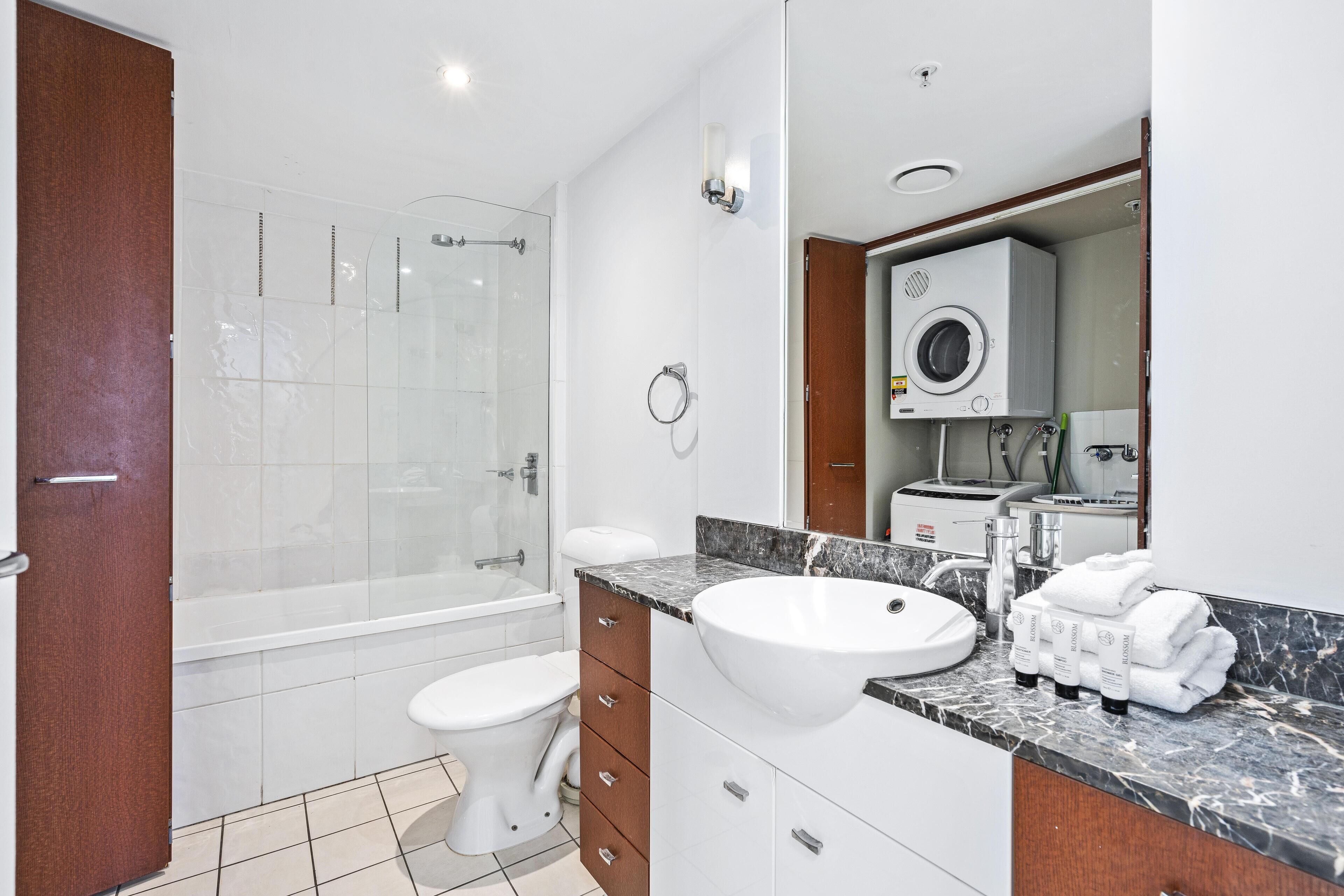 Une salle de bain moderne avec une douche à parois de verre, un lavabo blanc et un lave-linge encastré.