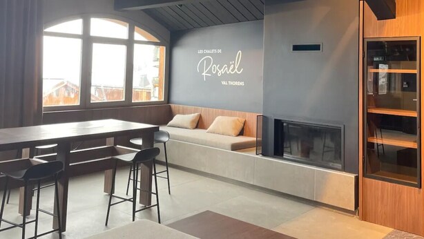 A modern living room with a large window, a fireplace, and a wall-mounted sign. - Luxury chalet apartment with ski-in/ski-out pool (Les Belleville)