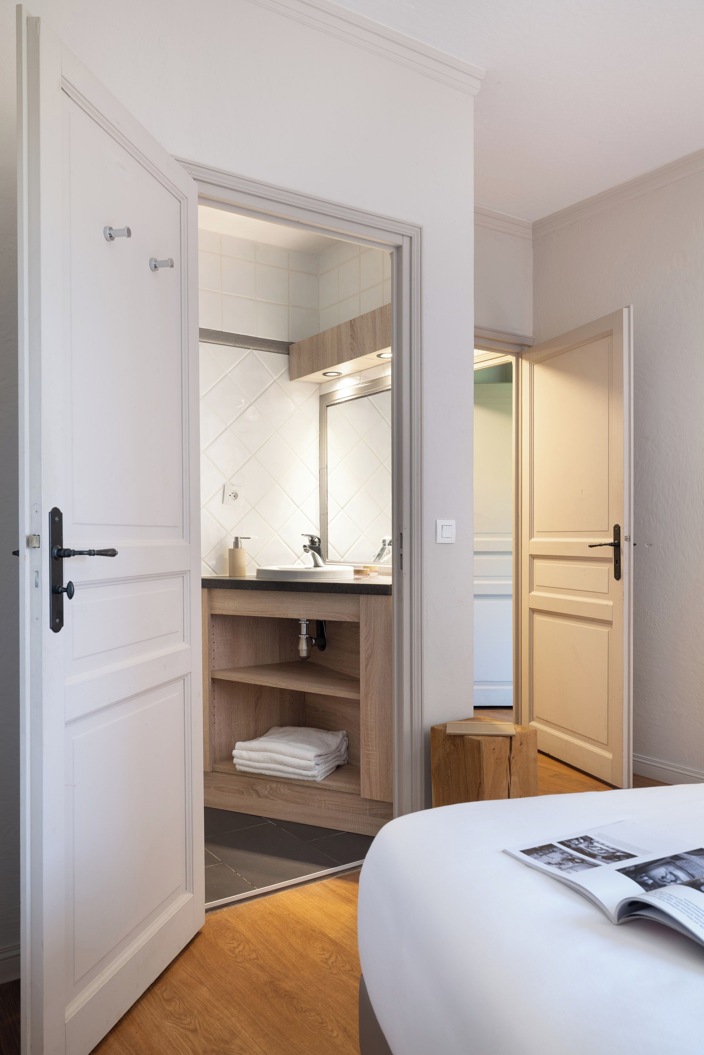 A bedroom with a bed, a magazine, a wooden stool, and a closet with a mirror and shelves.