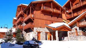 A multi-story wooden lodge with balconies, stone foundation, and snow-covered surroundings. - Luxury chalet apartment with ski-in/ski-out pool (Les Belleville)